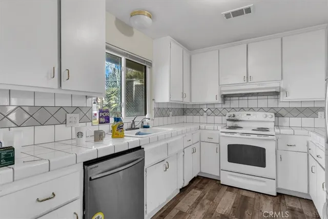 a kitchen with white cabinets appliances a sink and a window