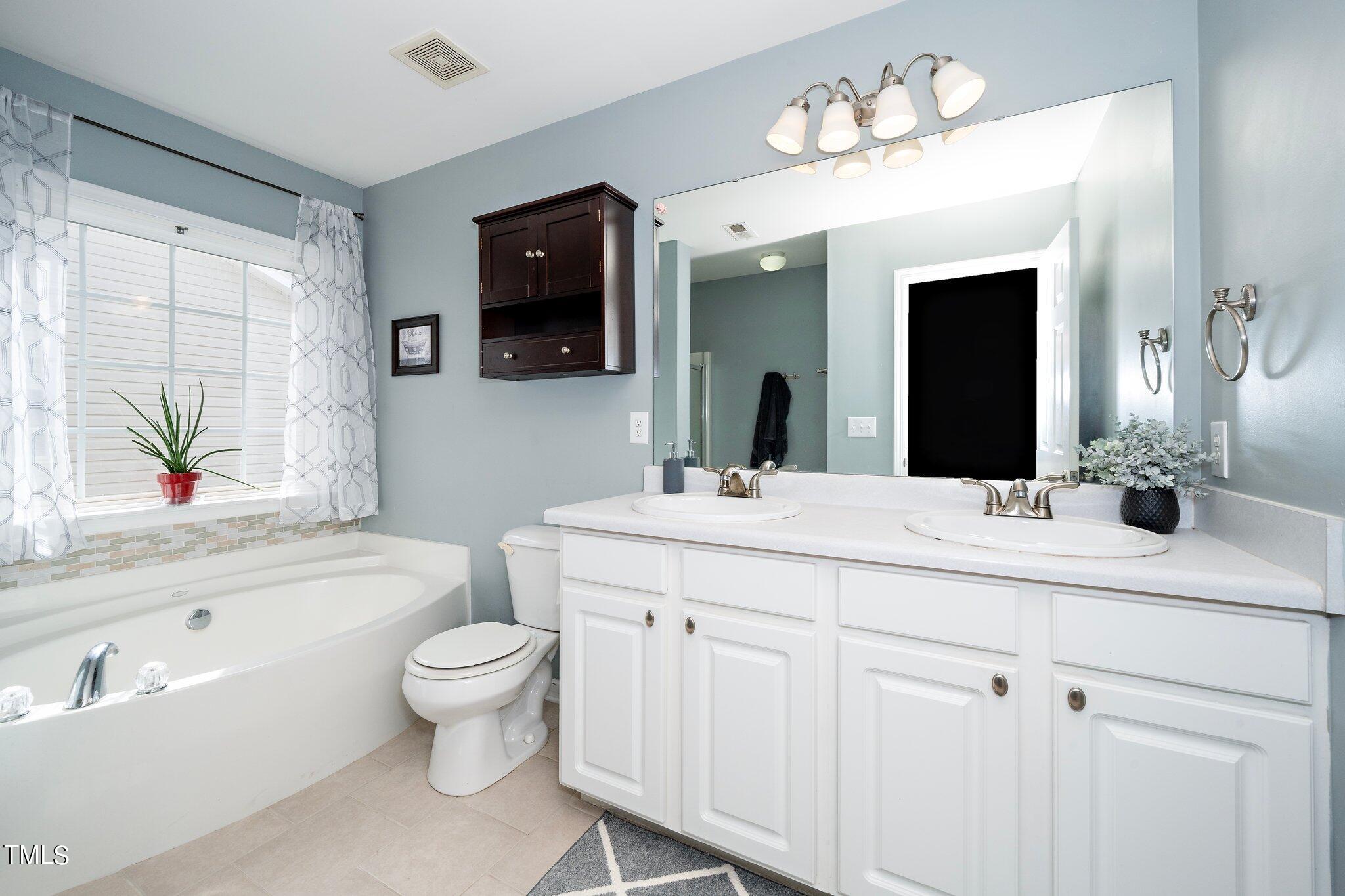 120 Solheim Lane Raleigh, NC 27603 - Photo 10 of 26 a bathroom with a double vanity sink a toilet a mirror and bathtub