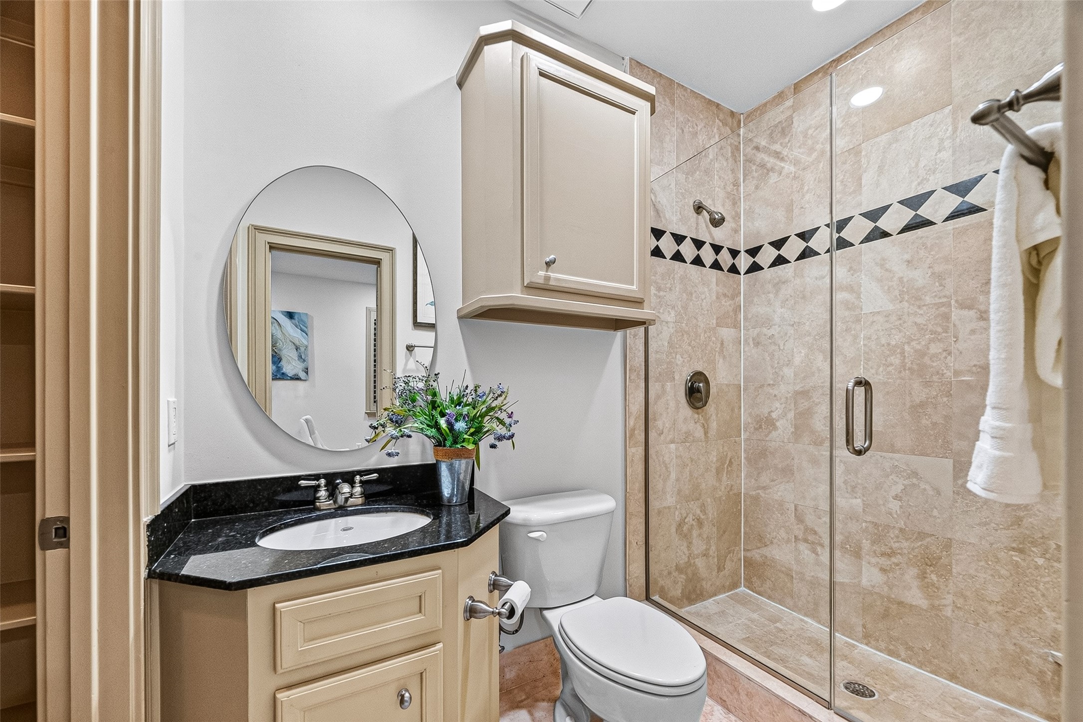 2034 Colquitt Street, Unit A Houston, TX 77098 - Photo 11 of 41 This first floor bathroom features a sleek design with a glass-enclosed shower, beige tile work, and a stylish black countertop. It includes built-in storage, a round mirror, and modern fixtures, offering a clean and functional space.