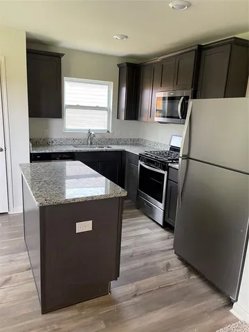 a kitchen with granite countertop a refrigerator a sink a stove and cabinets