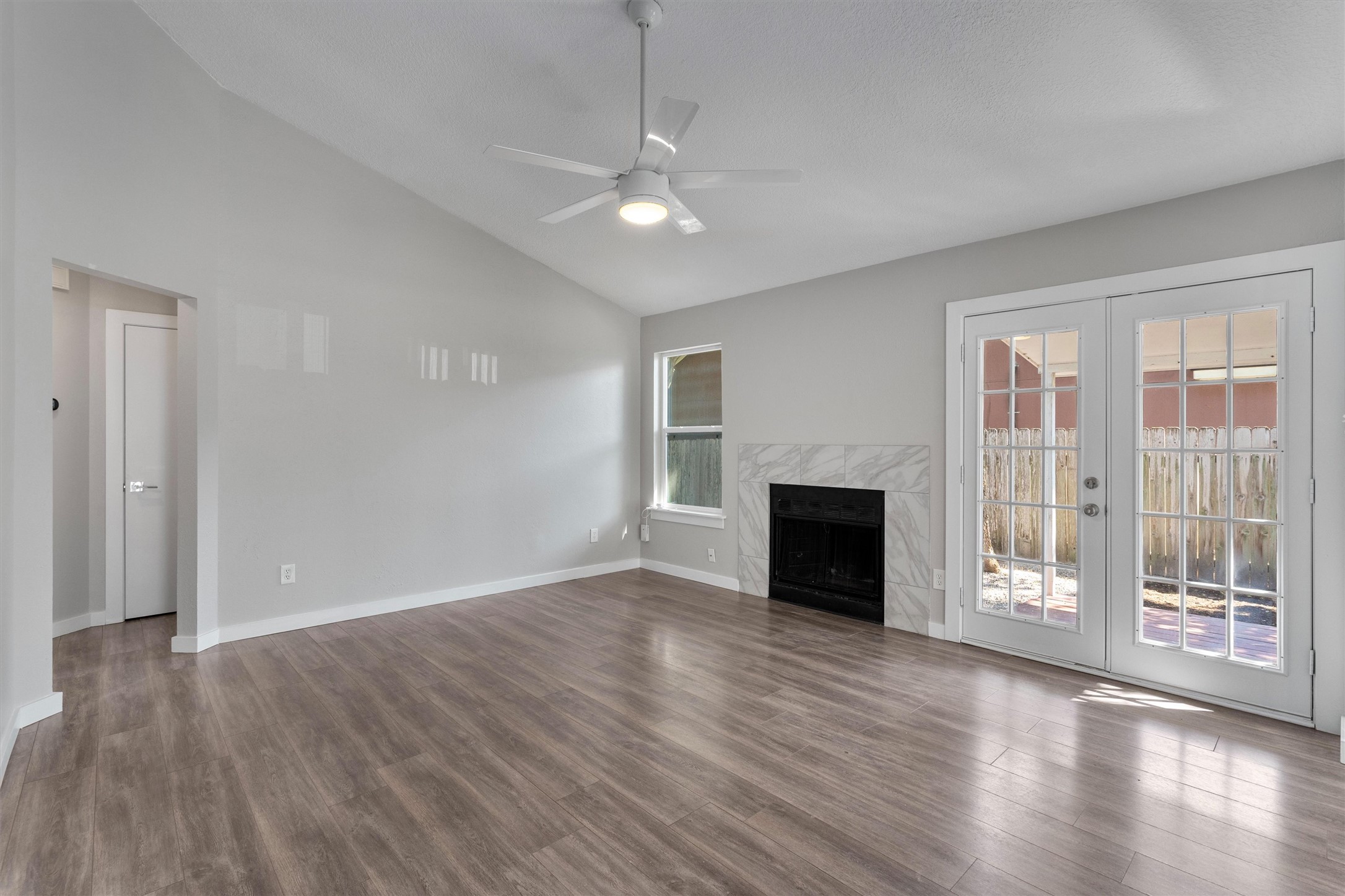 12321 Emery Oaks Road Austin, TX 78758 - Photo 5 of 27 A well-lit, spacious living space features vaulted ceilings, natural light, a cozy fireplace, and French doors leading to outdoor relaxation.