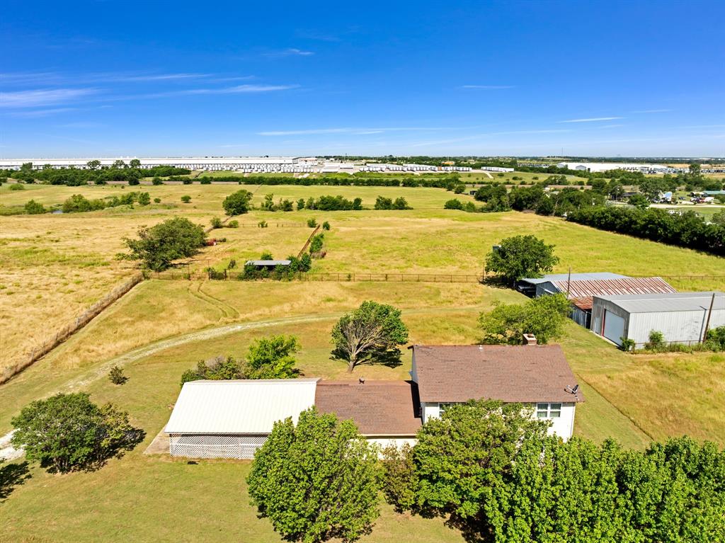 1795 Melton Road Sanger, TX 76266 - Photo 7 of 17 Expansive land featuring a single-story residence with a brown shingle roof, accompanied by multiple outbuildings including a large structure with a white metal roof and additional metal-sided structures