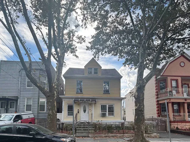 a front view of a house with trees and cars