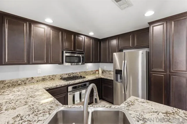 a kitchen with stainless steel appliances granite countertop a refrigerator a stove and a sink with wooden cabinets