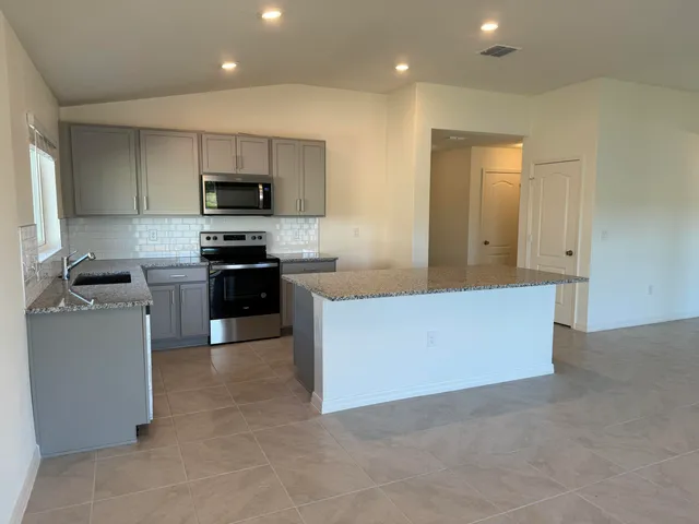 a large kitchen with stainless steel appliances granite countertop a stove top oven a sink a refrigerator and white cabinets