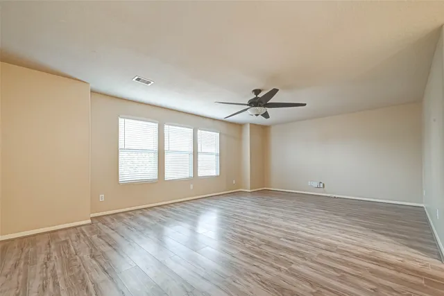 an empty room with wooden floor fan and windows