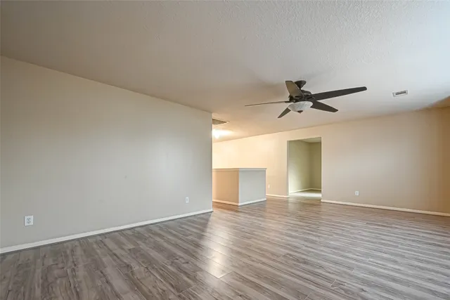 a view of an empty room with wooden floor and a ceiling fan