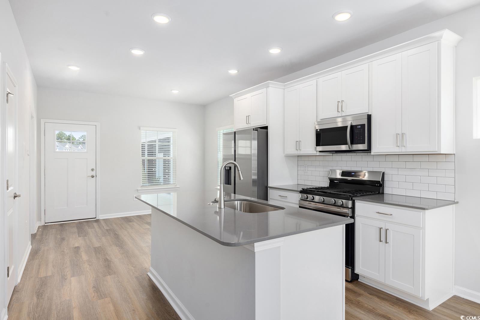283 Ferretti Street, Unit CONCORD Myrtle Beach, SC 29579 - Photo 18 of 34 Kitchen with stainless steel appliances, a sink, light wood-style flooring, tasteful backsplash, and a kitchen island with sink