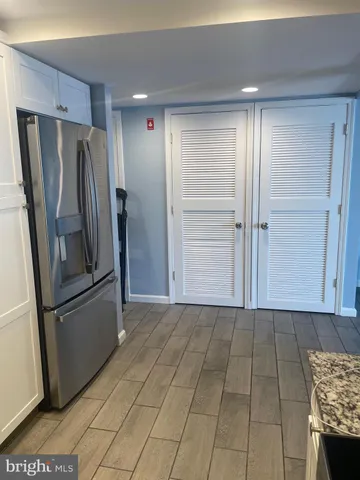 a view of a refrigerator in kitchen and an empty room in wooden floor