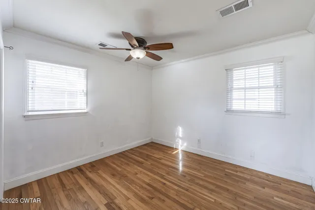 an empty room with wooden floor fan and windows