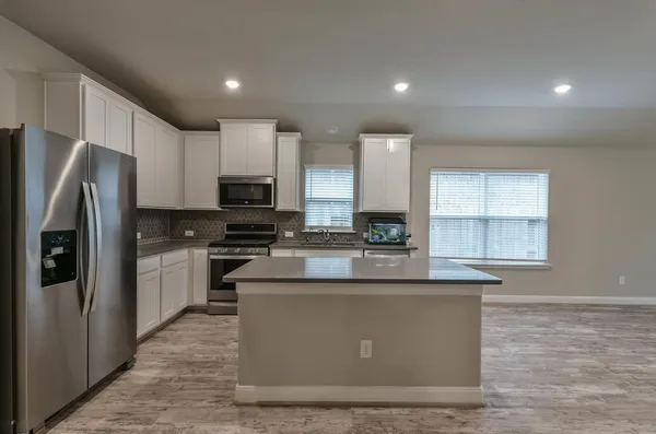 a kitchen with stainless steel appliances granite countertop a refrigerator a sink a stove a microwave and white cabinets