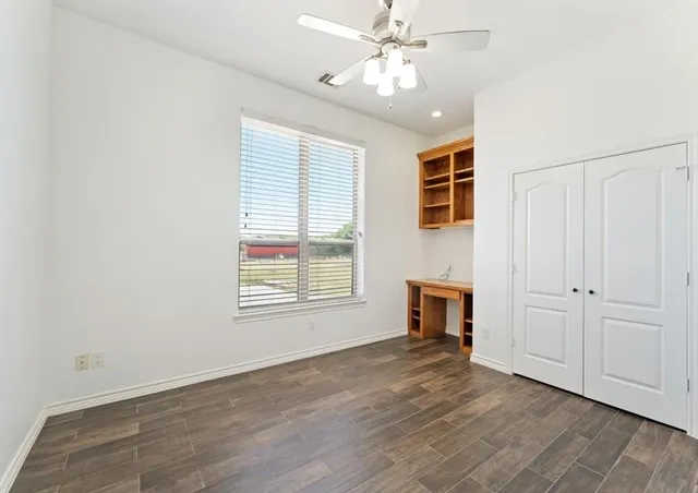 an empty room with wooden floor fan and windows