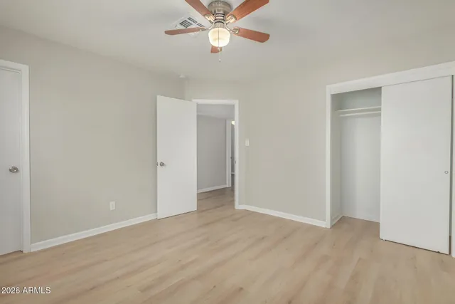 an empty room with wooden floor closet and fan