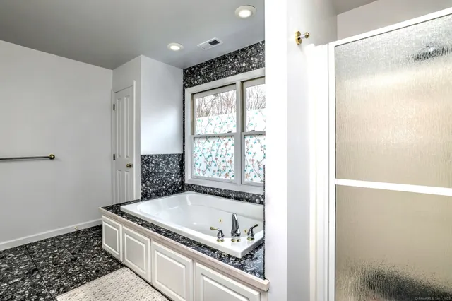 a bathroom with a granite countertop bathtub a shower and a window
