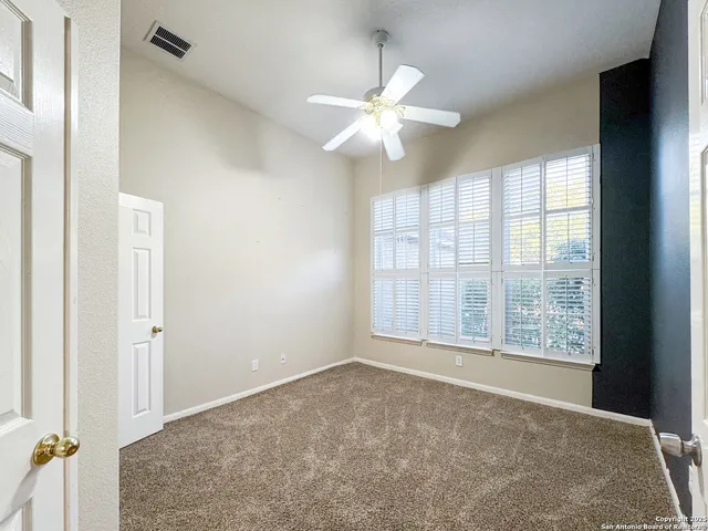 an empty room with chandelier fan and windows