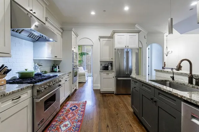 a kitchen with stainless steel appliances a refrigerator a stove a sink a dining table and chairs with wooden floor