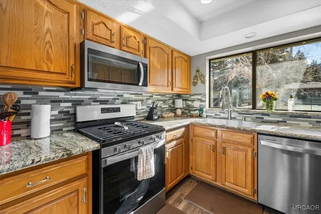 a kitchen with stainless steel appliances granite countertop a refrigerator a sink and white cabinets next to a window