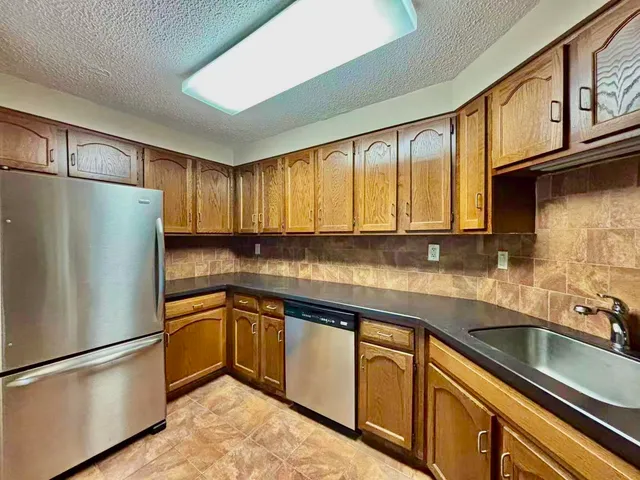 a kitchen with stainless steel appliances granite countertop a refrigerator a sink dishwasher a stove top oven and a dining table with wooden cabinet