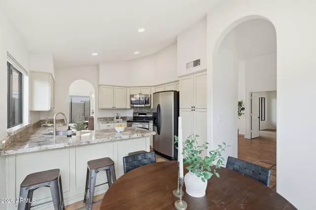 a kitchen with stainless steel appliances kitchen island granite countertop a refrigerator a sink dishwasher a dining table and chairs with wooden floor