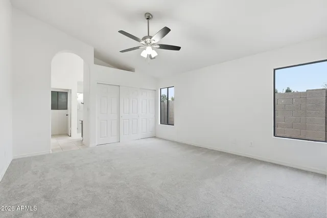 an empty room with chandelier fan and windows