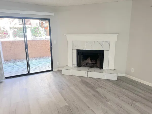 a view of an empty room with wooden floor fireplace and a window