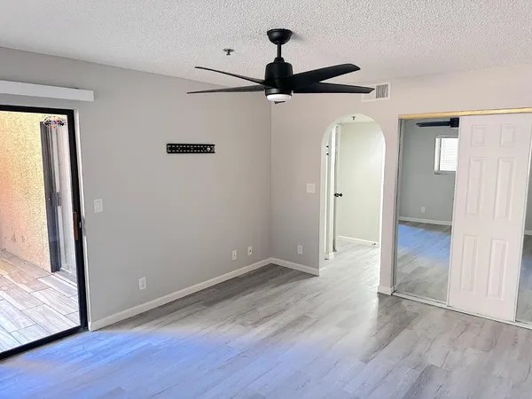 an empty room with wooden floor a ceiling fan and windows