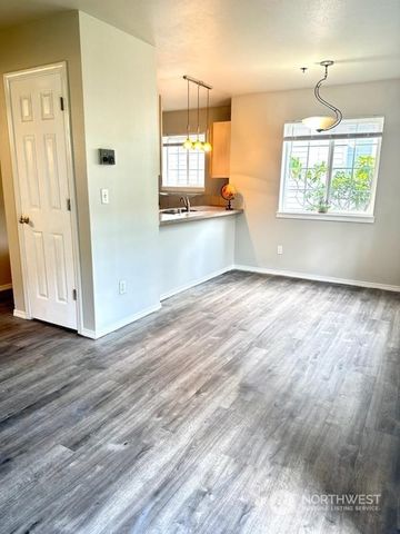 an empty room with wooden floor a kitchen view and windows