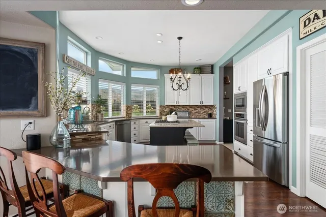 a kitchen with stainless steel appliances granite countertop a refrigerator a stove a sink a dining table and chairs with wooden floor