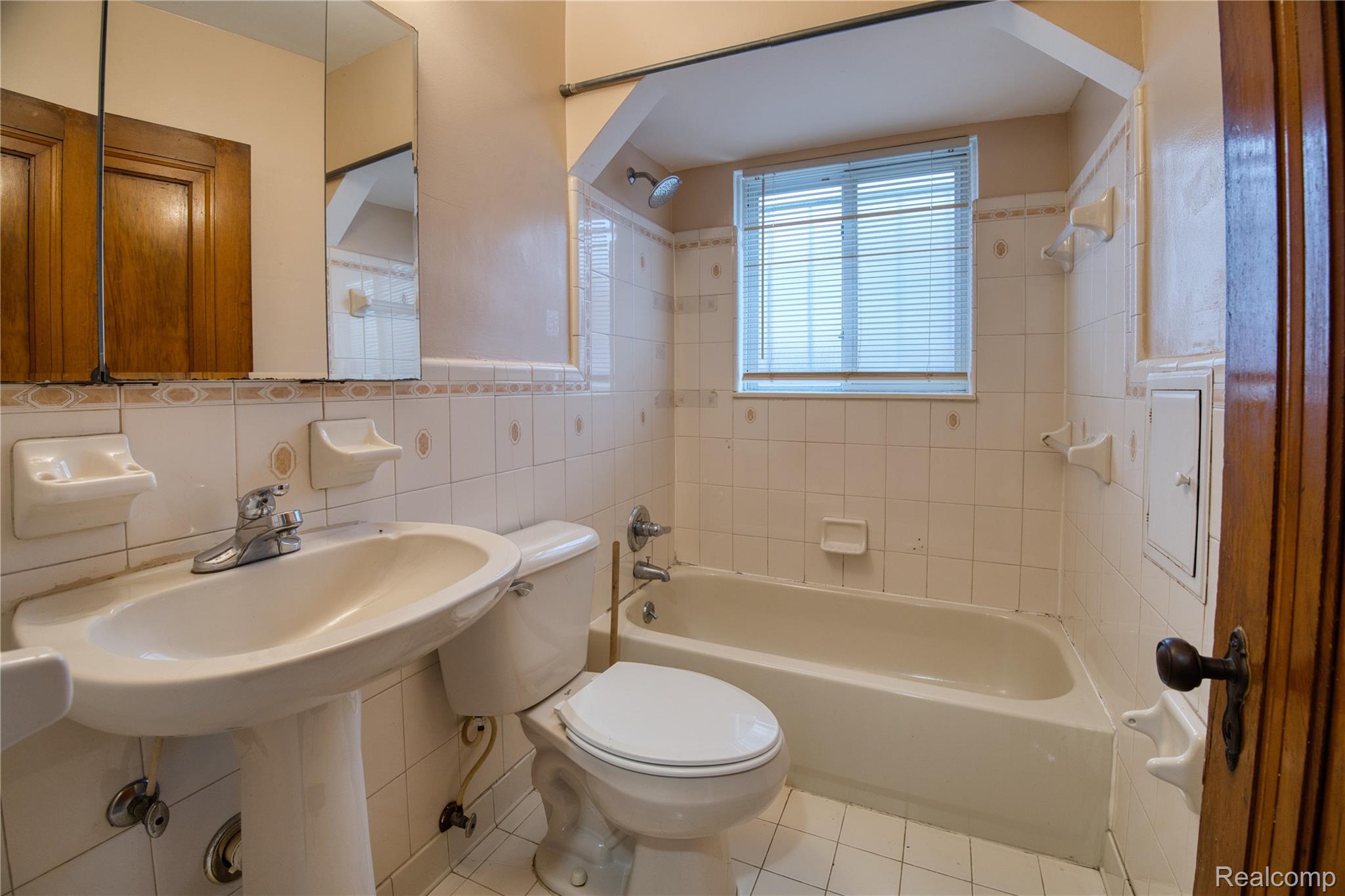 13644 Castleton Street Detroit, MI 48227 - Photo 7 of 18 Pedestal sink, ceramic tile flooring, ceramic tiled walls, built-in bathtub, and window with blinds