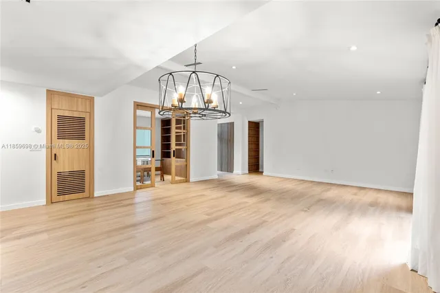 an empty room with wooden floor chandelier and windows