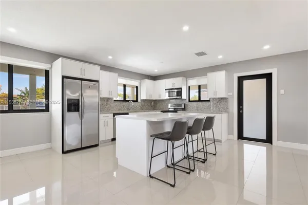 a kitchen with stainless steel appliances kitchen island granite countertop a refrigerator a stove a sink a dining table and chairs