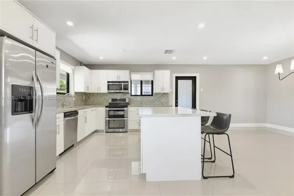 a kitchen with stainless steel appliances kitchen island granite countertop a refrigerator a stove top oven a sink dishwasher and white cabinets with wooden floor