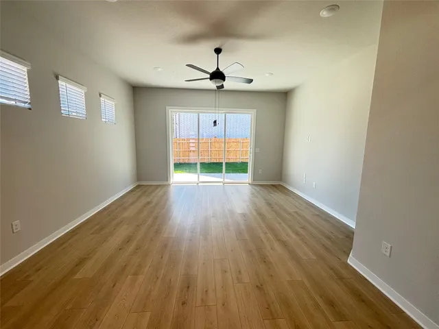 an empty room with wooden floor chandelier fan and windows