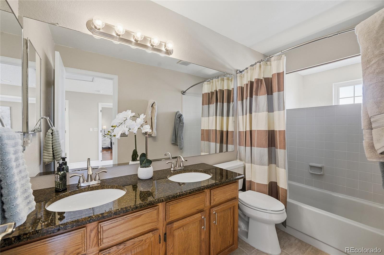 9264 Madras Court Highlands Ranch, CO 80130 - Photo 27 of 50 a bathroom with a granite countertop sink toilet a mirror a bathtub and shower