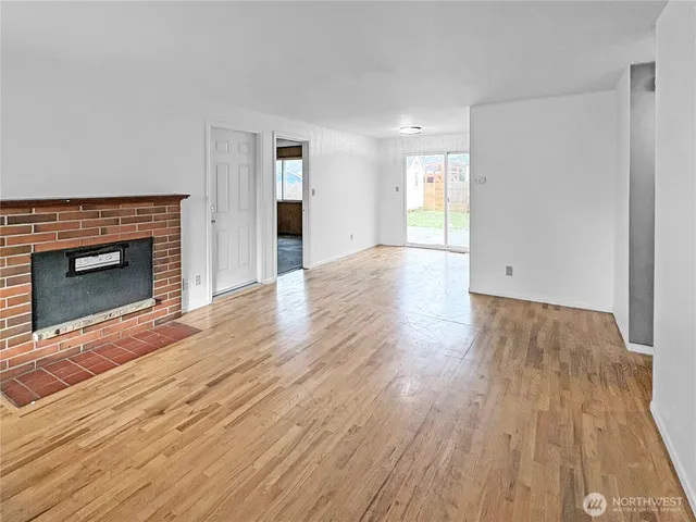 an empty room with wooden floor fireplace and windows