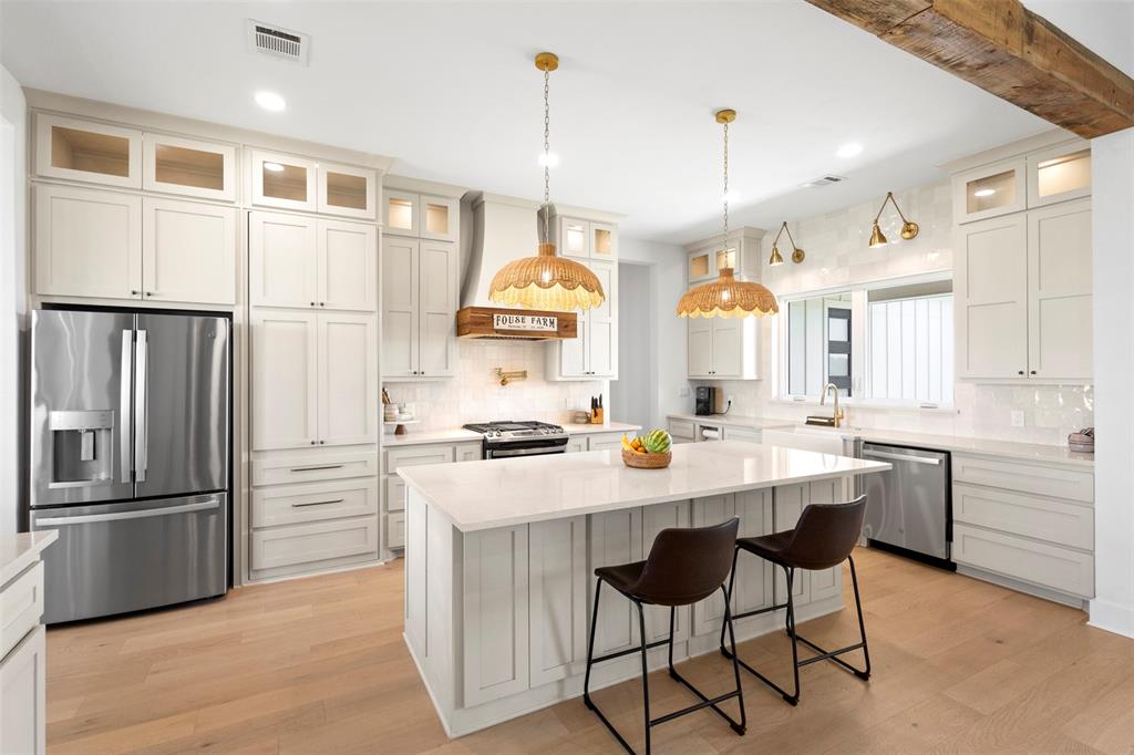 861 Brindley Road Maypearl, TX 76064 - Photo 13 of 36 Kitchen featuring a large island with seating, stainless steel appliances, extensive cabinetry with glass-front uppers, wood-finish flooring, and a decorative exposed beam