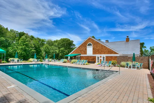 a view of swimming pool that has lawn chairs with plants and large trees