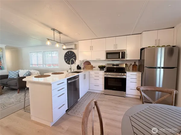 a kitchen with stainless steel appliances granite countertop a stove top oven a sink dishwasher a refrigerator and a dining table with wooden floor