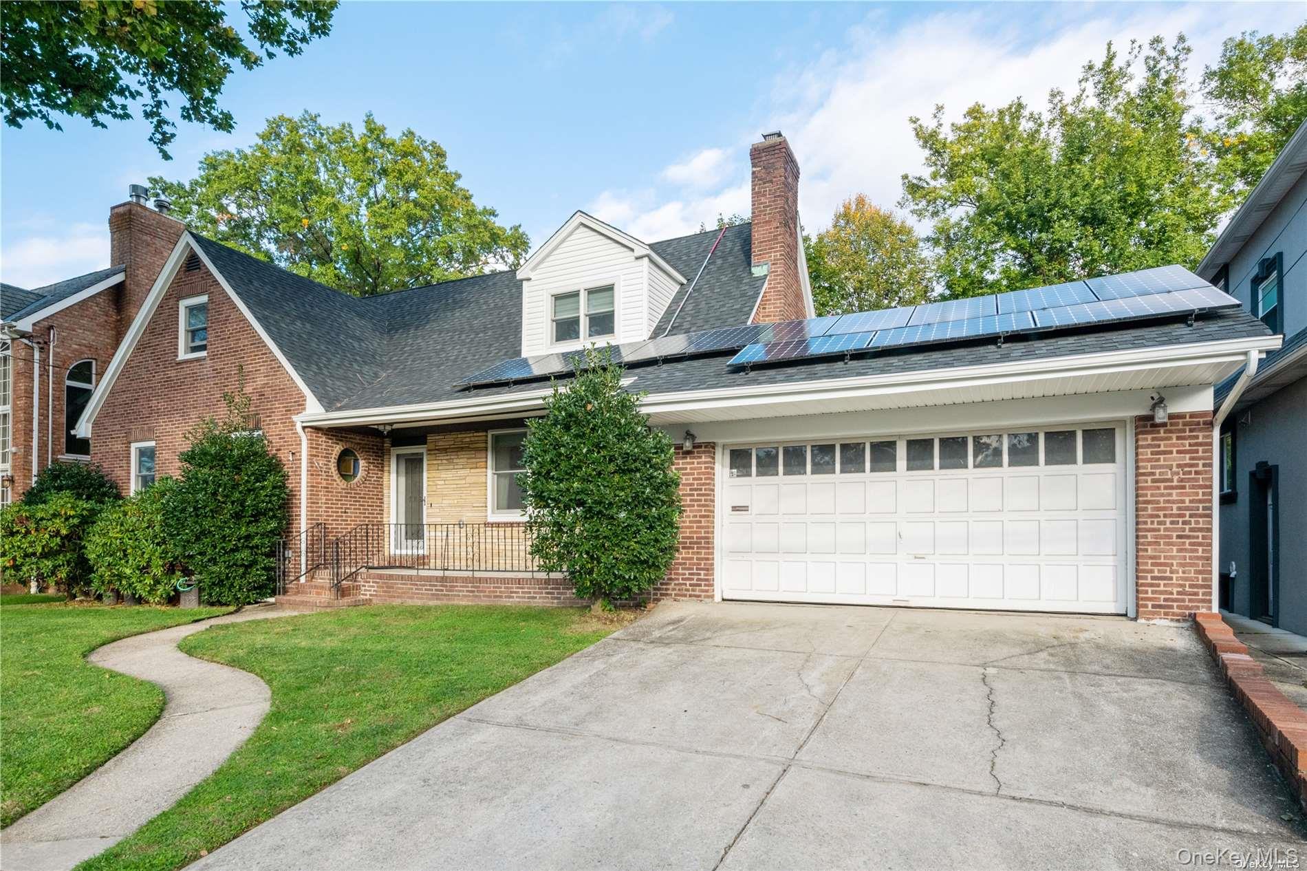 View of front facade with covered porch, brick siding, a front yard, a chimney, and concrete driveway