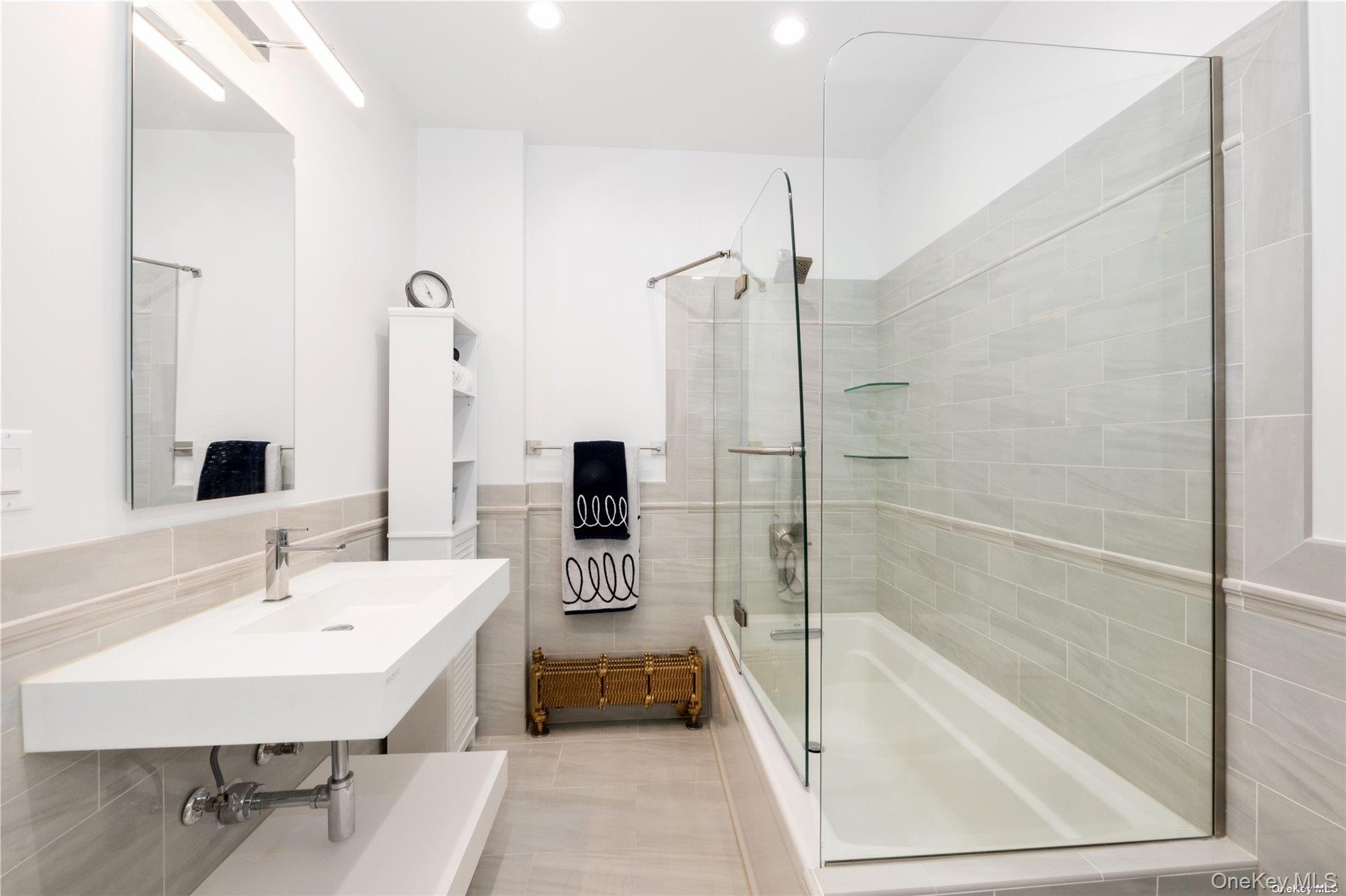 29-33 212th Street, Unit 1F Queens, NY 11360 - Photo 9 of 14 Bathroom featuring shower / bath combination with glass door, tile walls, light tile patterned floors, and a wainscoted wall