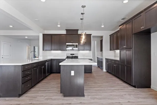 a large kitchen with stainless steel appliances kitchen island granite countertop wooden floors wooden cabinets and sink