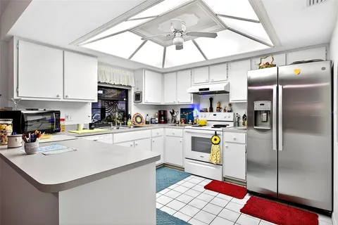 a kitchen with stainless steel appliances granite countertop a refrigerator a sink dishwasher a stove and white cabinets with wooden floor