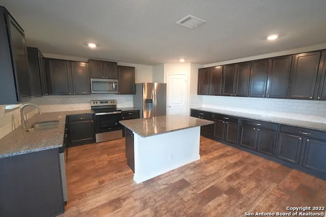 a large kitchen with kitchen island granite countertop a sink and a stove top oven