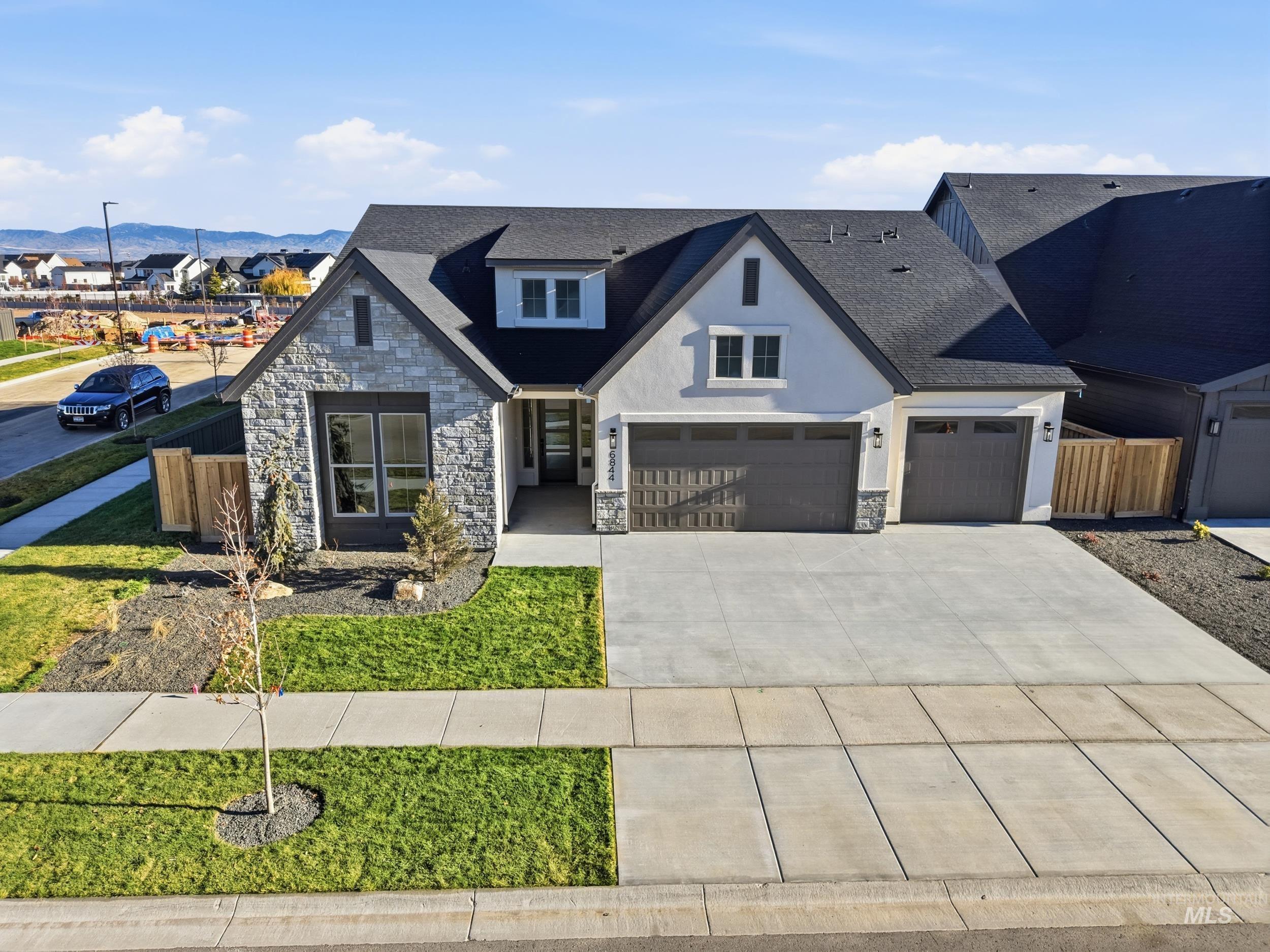 Modern farmhouse featuring stone siding, roof with shingles, concrete driveway, and a garage