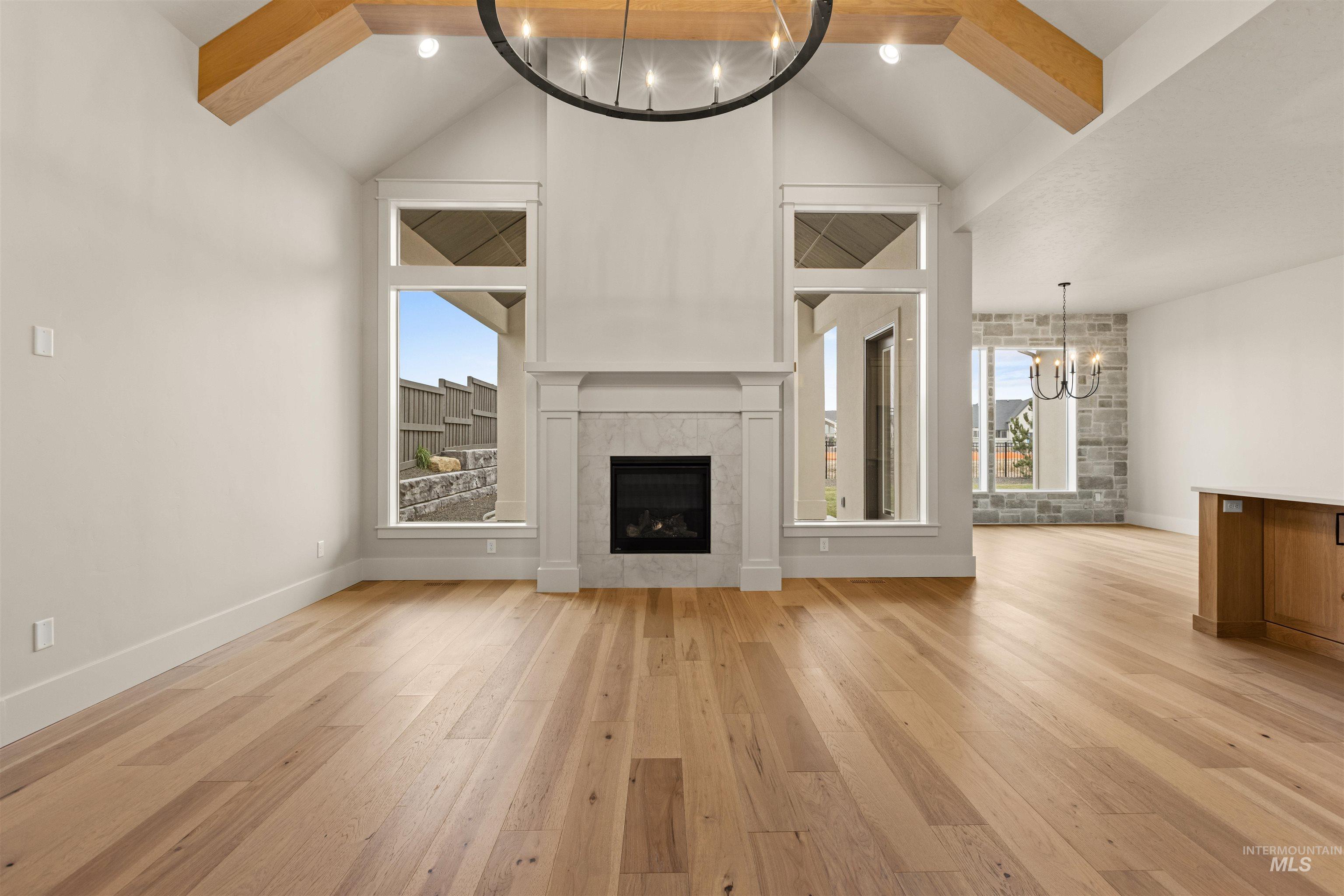 6844 South Messner Way Meridian, ID 83642 - Photo 12 of 49 Unfurnished living room with a chandelier, beamed ceiling, light wood finished floors, high vaulted ceiling, and a tiled fireplace