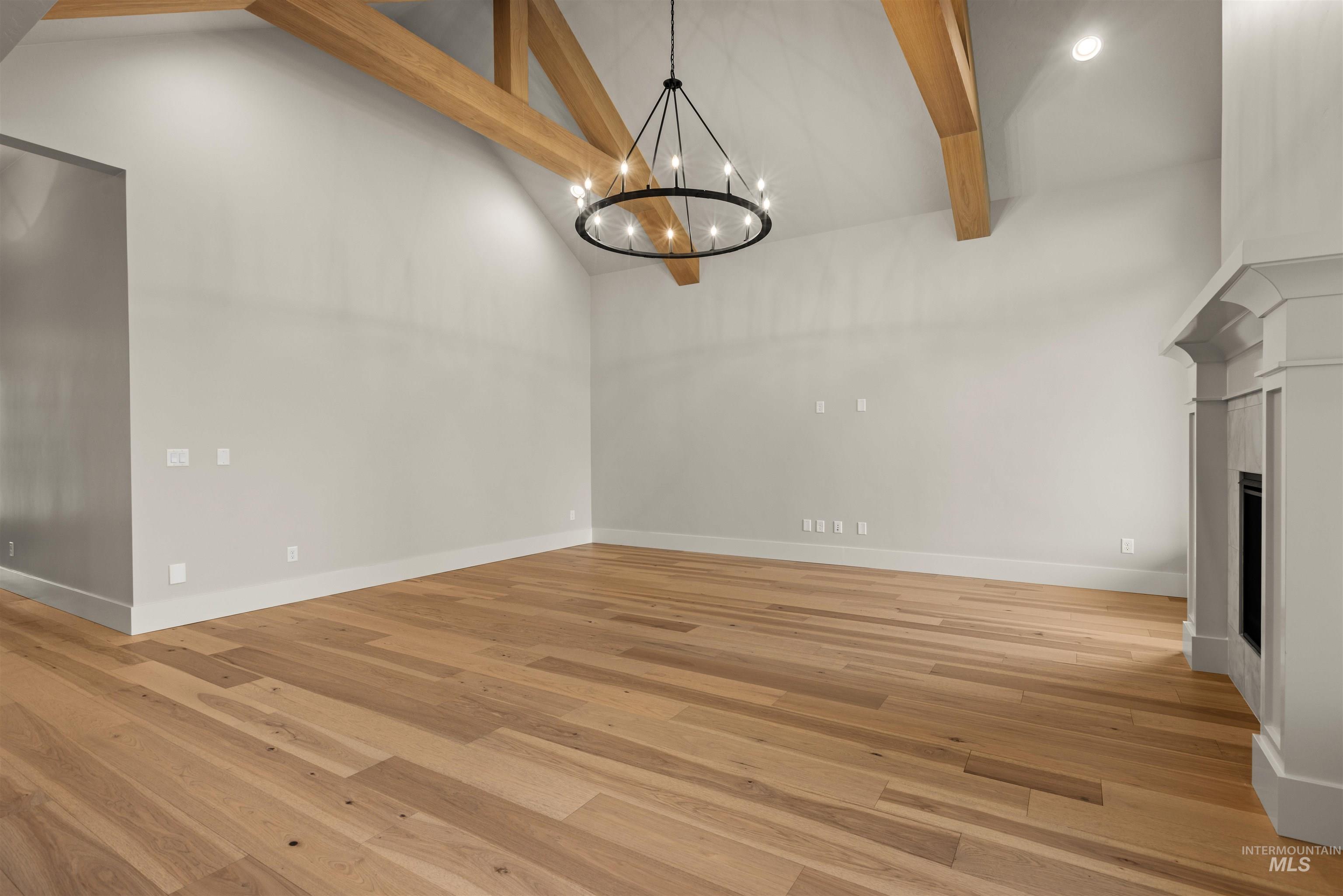 6844 South Messner Way Meridian, ID 83642 - Photo 13 of 49 Unfurnished living room featuring beam ceiling, high vaulted ceiling, light wood-style flooring, a chandelier, and a fireplace