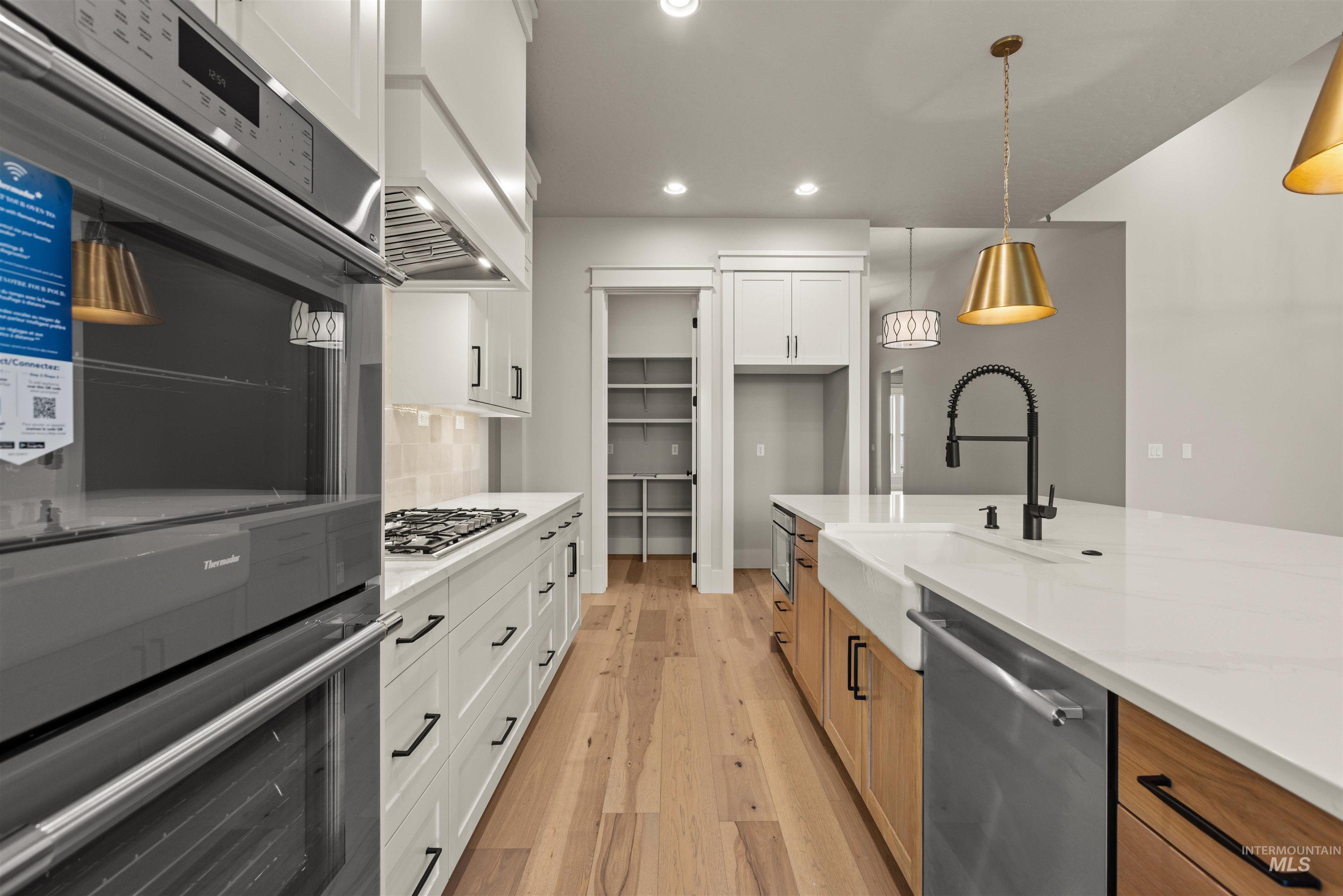 6844 South Messner Way Meridian, ID 83642 - Photo 15 of 49 Kitchen featuring appliances with stainless steel finishes, white cabinetry, recessed lighting, light wood-type flooring, and pendant lighting