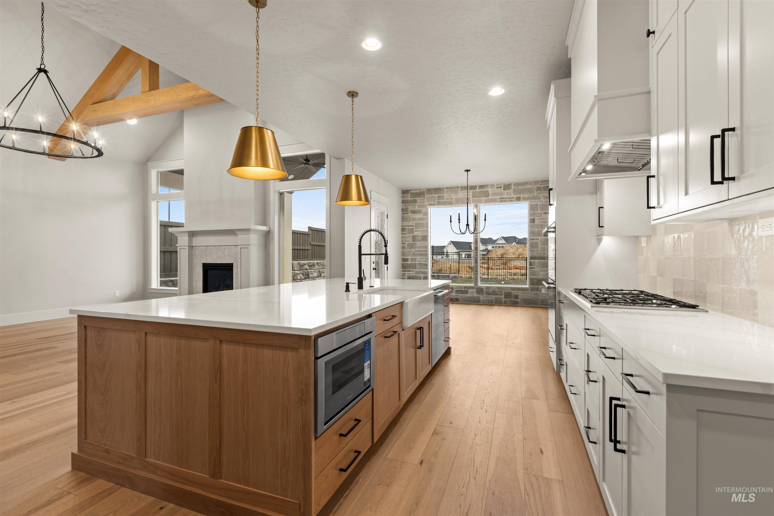 6844 South Messner Way Meridian, ID 83642 - Photo 17 of 49 Kitchen with a chandelier, white cabinetry, light wood-type flooring, a tiled fireplace, and pendant lighting