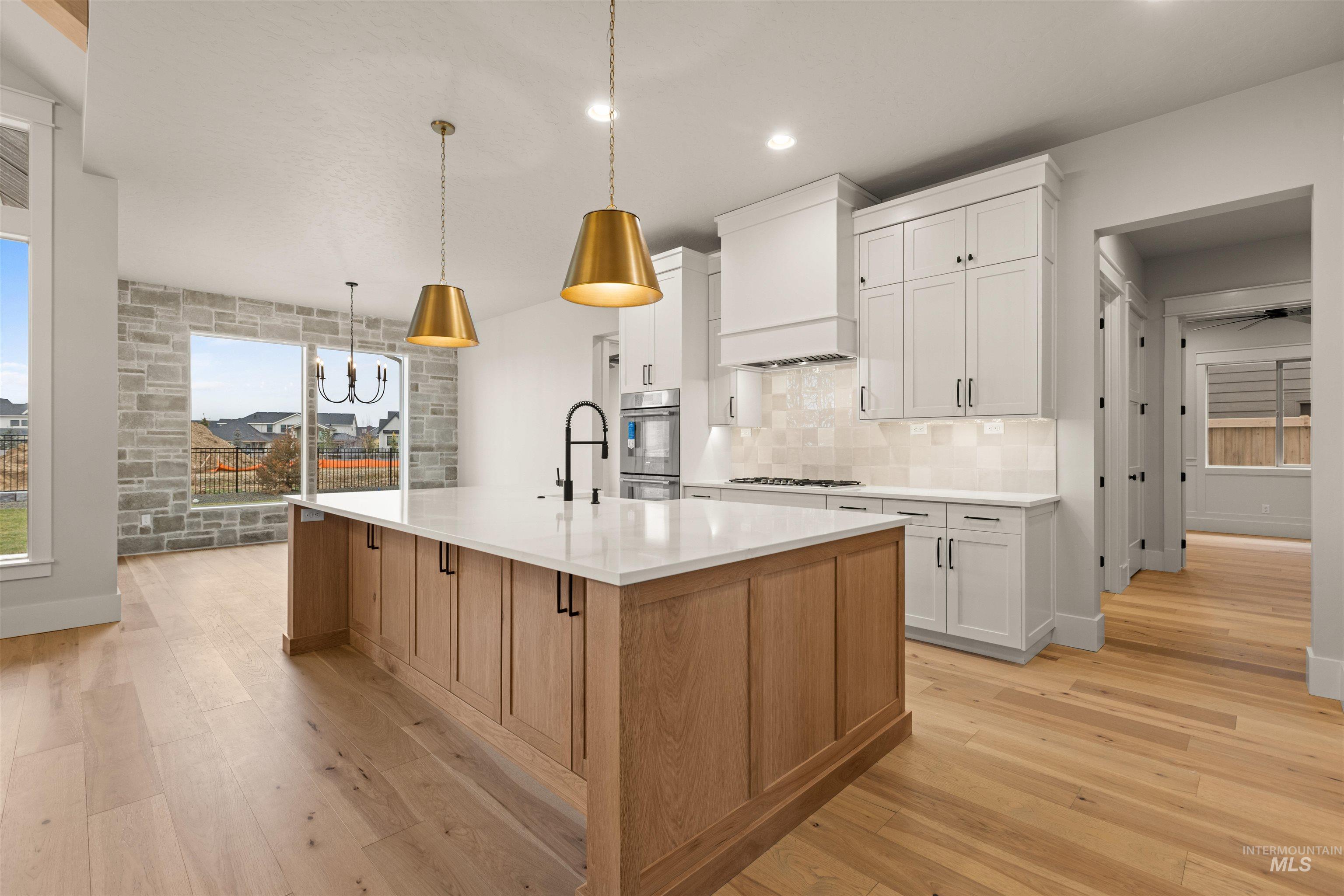 6844 South Messner Way Meridian, ID 83642 - Photo 18 of 49 Kitchen featuring white cabinets, light wood-type flooring, tasteful backsplash, a kitchen island with sink, and hanging light fixtures