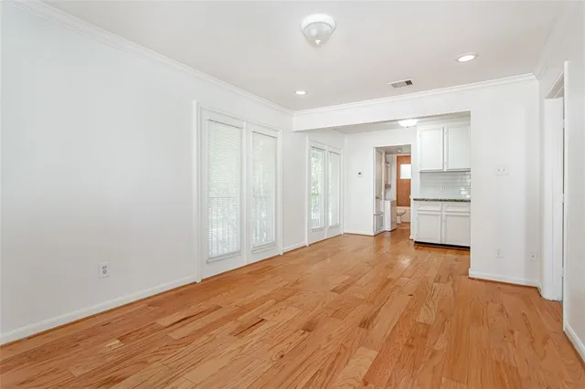 a view of empty room with wooden floor and kitchen